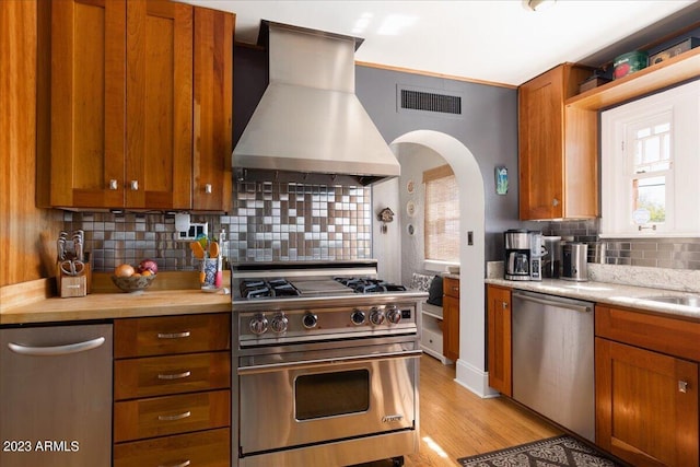 kitchen featuring wall chimney range hood, backsplash, and appliances with stainless steel finishes