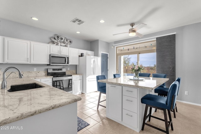 kitchen featuring light stone counters, stainless steel appliances, a kitchen bar, white cabinetry, and a sink