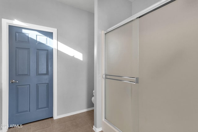 bathroom with toilet, a shower stall, baseboards, and tile patterned floors