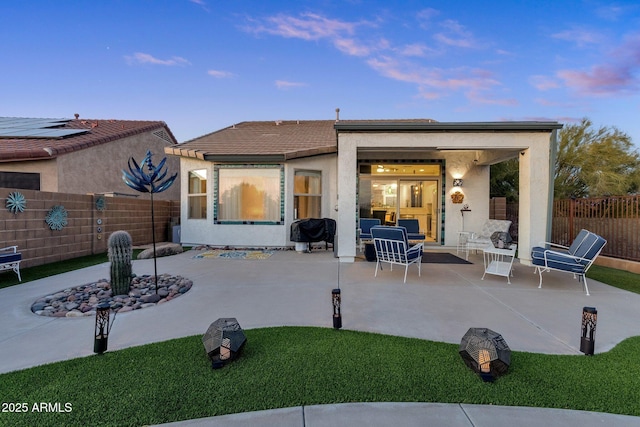 back of property at dusk featuring a patio, a fenced backyard, and stucco siding