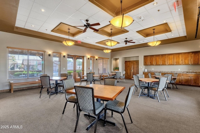 dining space with a tray ceiling, light carpet, ceiling fan, and a high ceiling