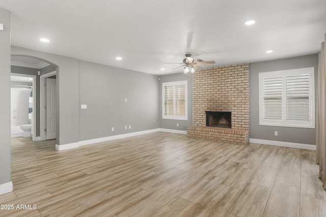 unfurnished living room with ceiling fan, arched walkways, baseboards, and recessed lighting