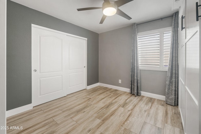 unfurnished bedroom featuring light wood-style flooring, a closet, baseboards, and ceiling fan