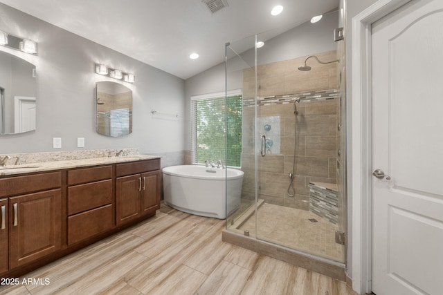 full bath with vaulted ceiling, a freestanding bath, a shower stall, double vanity, and recessed lighting