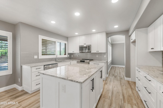 kitchen featuring appliances with stainless steel finishes, baseboards, arched walkways, light wood-style floors, and tasteful backsplash