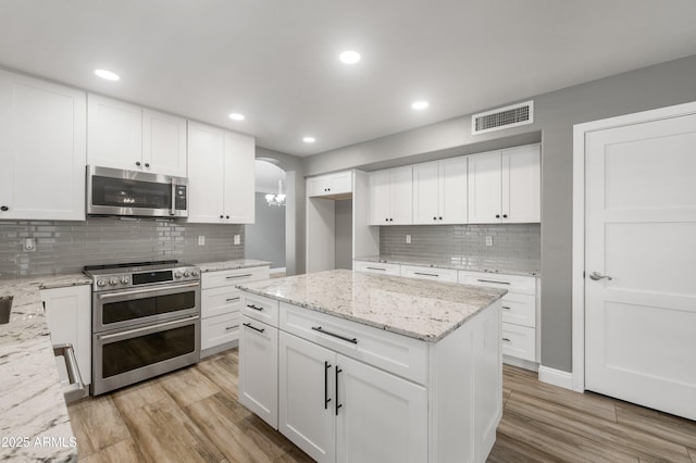 kitchen featuring stainless steel appliances, light wood-type flooring, decorative backsplash, arched walkways, and white cabinets