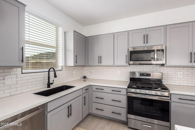 kitchen featuring a sink, light countertops, appliances with stainless steel finishes, backsplash, and gray cabinets