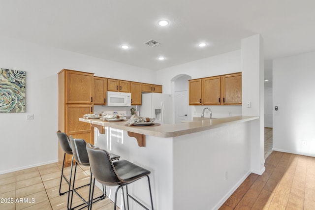 kitchen with white appliances, kitchen peninsula, a kitchen bar, light wood-type flooring, and sink