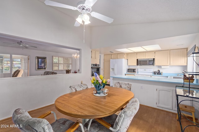 dining room featuring ceiling fan with notable chandelier, hardwood / wood-style flooring, and high vaulted ceiling