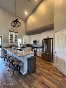 kitchen with high vaulted ceiling, appliances with stainless steel finishes, white cabinetry, and dark hardwood / wood-style floors