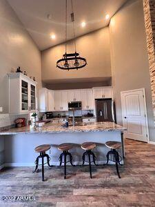 kitchen with high vaulted ceiling, hanging light fixtures, black refrigerator, and white cabinetry