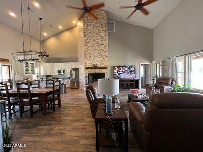 living room with high vaulted ceiling, dark hardwood / wood-style flooring, ceiling fan, and a stone fireplace