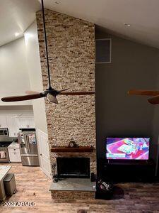 living room with vaulted ceiling, ceiling fan, a fireplace, and wood-type flooring