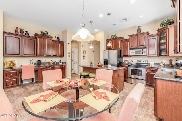 kitchen with hanging light fixtures, stainless steel appliances, a center island, built in desk, and dark stone counters