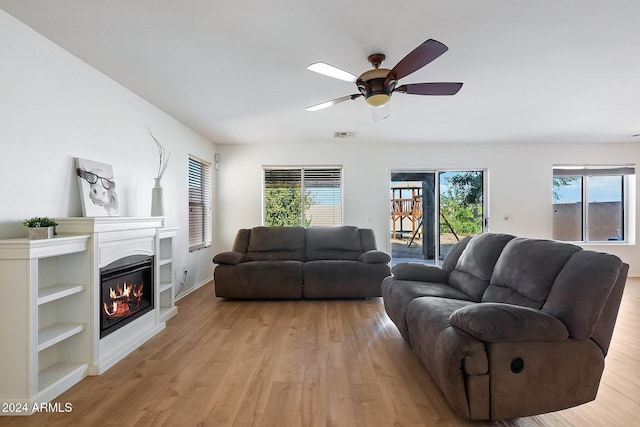 living room featuring visible vents, light wood-type flooring, a glass covered fireplace, and a ceiling fan