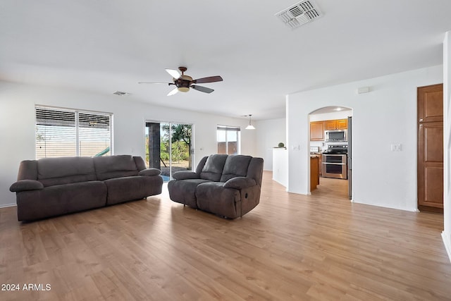 living room featuring arched walkways, ceiling fan, visible vents, and light wood-style floors