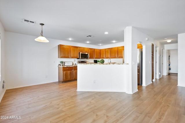 kitchen featuring light wood-style flooring, stainless steel microwave, visible vents, and brown cabinets