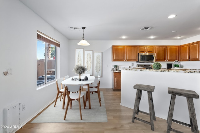 kitchen featuring stainless steel microwave, hanging light fixtures, light wood-style flooring, visible vents, and brown cabinetry