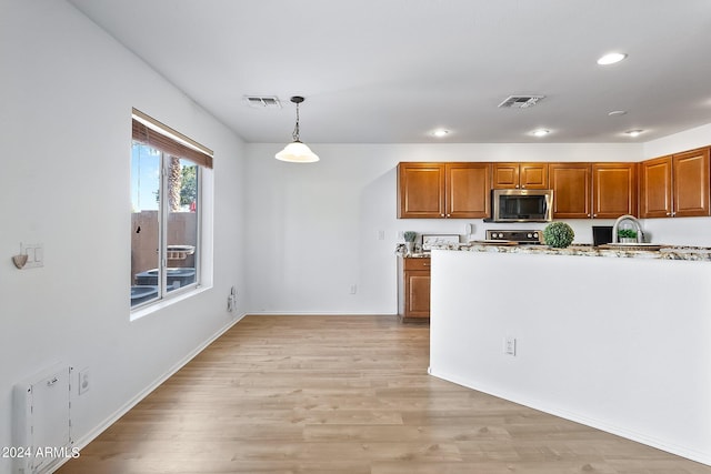 kitchen with pendant lighting, stainless steel microwave, visible vents, light wood-style floors, and brown cabinetry