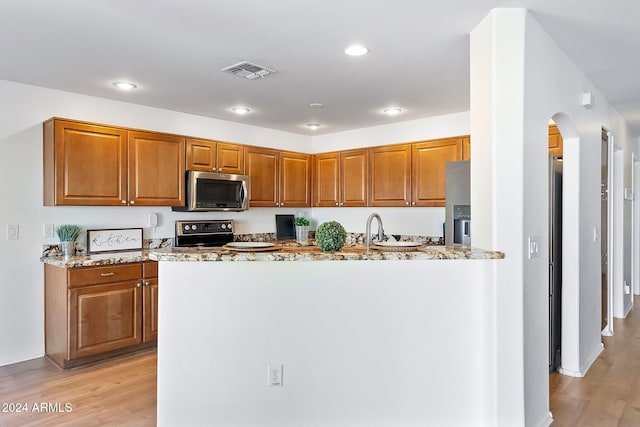 kitchen with light stone counters, stainless steel appliances, visible vents, brown cabinetry, and light wood-style floors