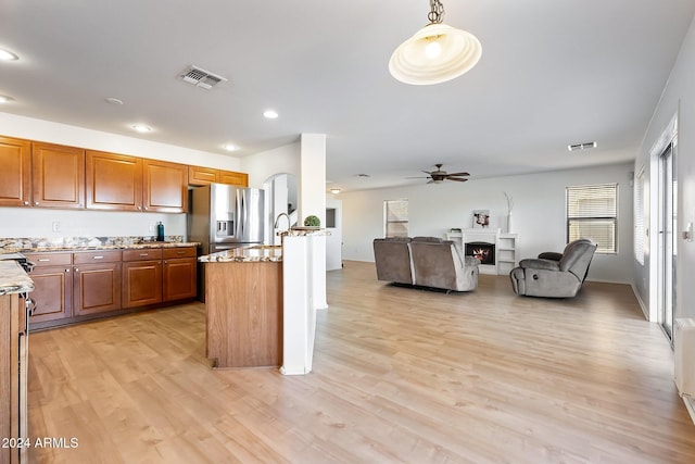 kitchen featuring a warm lit fireplace, visible vents, stainless steel fridge with ice dispenser, brown cabinets, and light wood finished floors