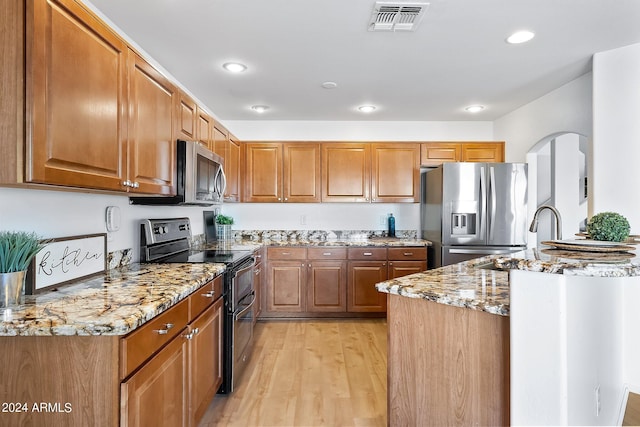 kitchen featuring light wood finished floors, visible vents, brown cabinetry, appliances with stainless steel finishes, and light stone countertops