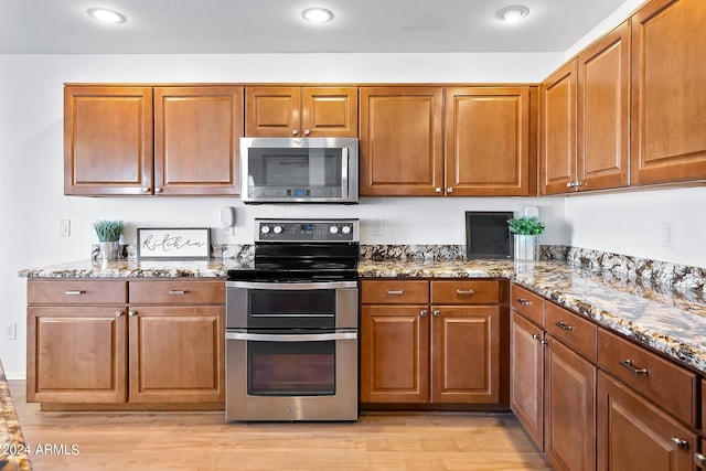 kitchen with appliances with stainless steel finishes, stone countertops, brown cabinetry, and light wood-style floors