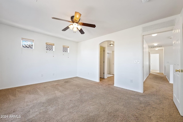 carpeted empty room with arched walkways, visible vents, a ceiling fan, and baseboards