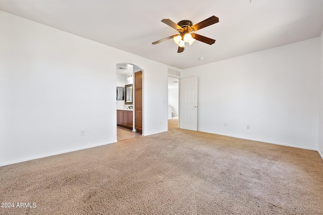 unfurnished bedroom with arched walkways, connected bathroom, light colored carpet, visible vents, and baseboards