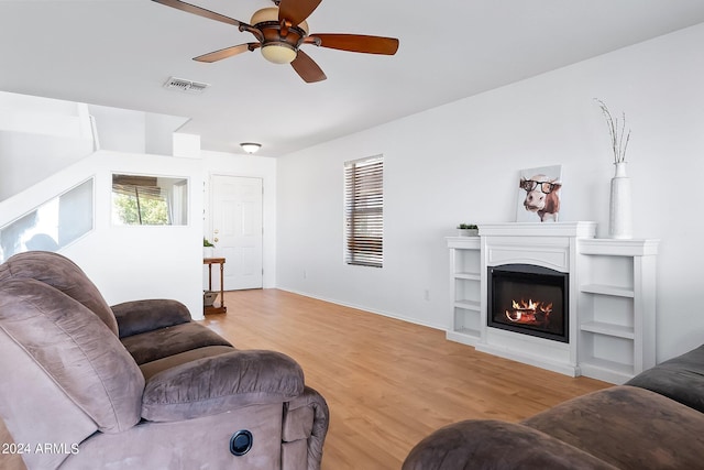 living room with baseboards, visible vents, a ceiling fan, a glass covered fireplace, and light wood-style floors