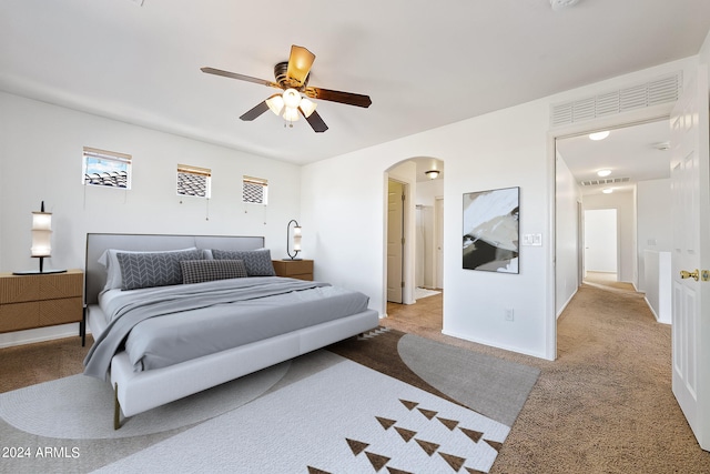 carpeted bedroom with arched walkways, baseboards, visible vents, and a ceiling fan