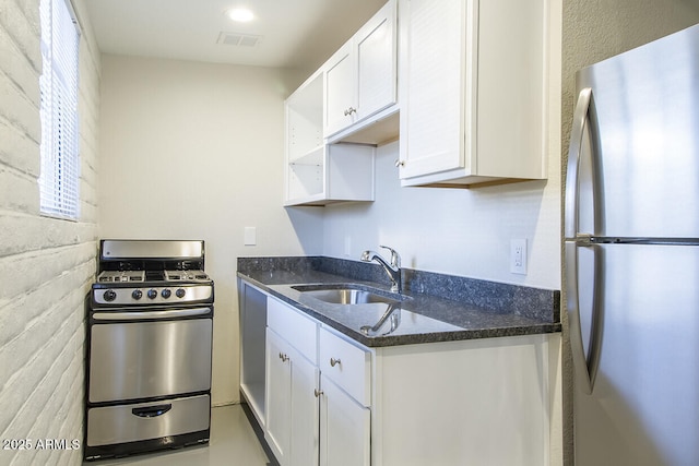 kitchen featuring sink, appliances with stainless steel finishes, white cabinets, dark stone counters, and brick wall