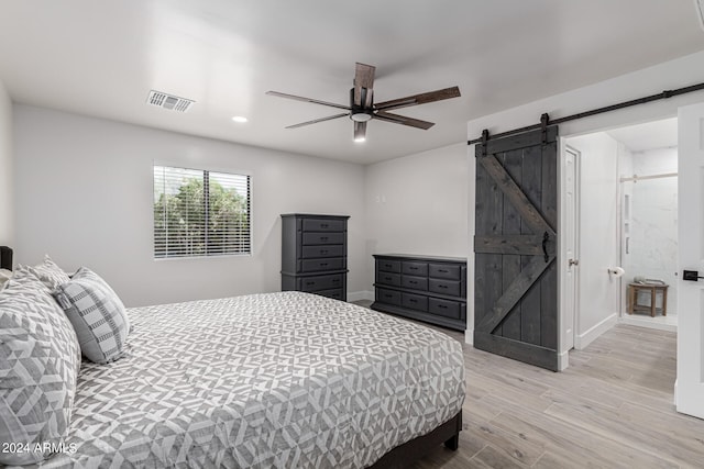 bedroom with a barn door, ceiling fan, and light hardwood / wood-style flooring