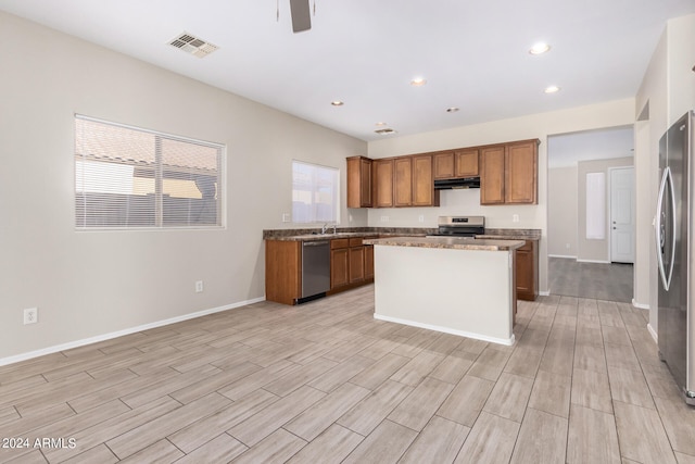 kitchen with stainless steel appliances, light hardwood / wood-style floors, a kitchen island, and ceiling fan