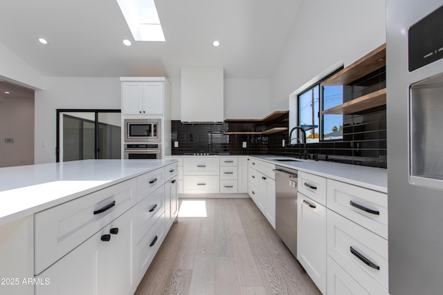 kitchen with stainless steel appliances, a sink, open shelves, a skylight, and backsplash