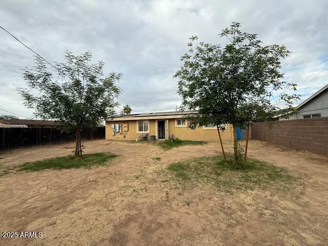 rear view of house with roof mounted solar panels and a fenced backyard