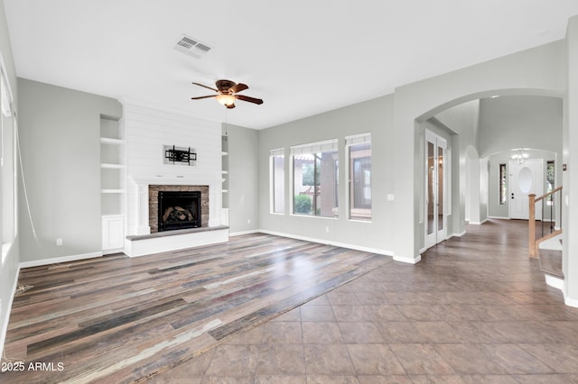 18544 E Caledonia Dr, Queen Creek, AZ 85142 - unfurnished living room with visible vents, a fireplace with raised hearth, a ceiling fan, built in features, and arched walkways