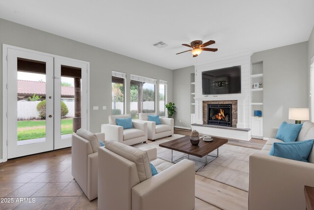 18544 E Caledonia Dr, Queen Creek, AZ 85142 - living area featuring visible vents, built in shelves, ceiling fan, a warm lit fireplace, and french doors