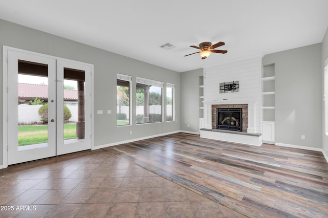 18544 E Caledonia Dr, Queen Creek, AZ 85142 - unfurnished living room with visible vents, a fireplace with raised hearth, baseboards, ceiling fan, and built in features
