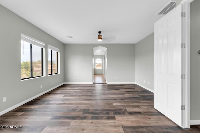 18544 E Caledonia Dr, Queen Creek, AZ 85142 - empty room with dark wood-style floors, arched walkways, visible vents, and baseboards