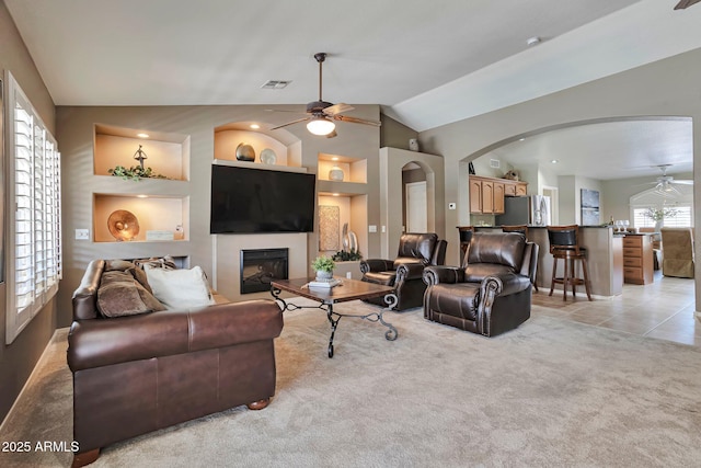 2984 N 152nd Dr, Goodyear, AZ 85395 - living area featuring a ceiling fan, arched walkways, a glass covered fireplace, vaulted ceiling, and light carpet