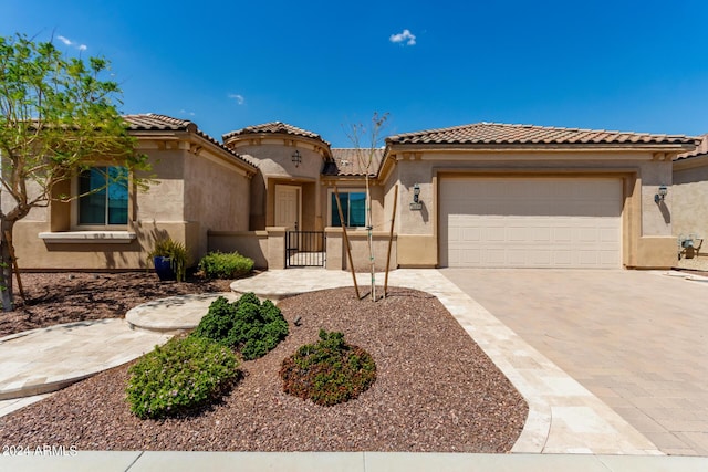 mediterranean / spanish home with a gate, decorative driveway, an attached garage, and stucco siding