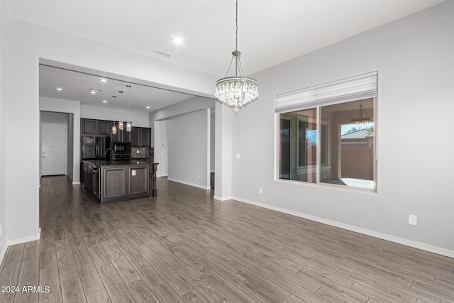 unfurnished living room with baseboards, visible vents, a chandelier, and wood finished floors