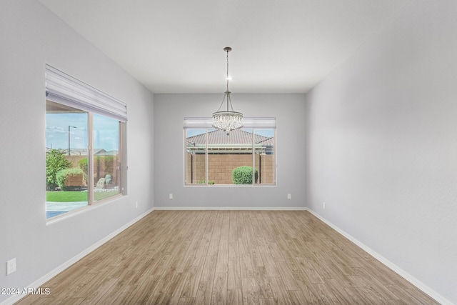 unfurnished room with a chandelier, wood finished floors, a wealth of natural light, and baseboards