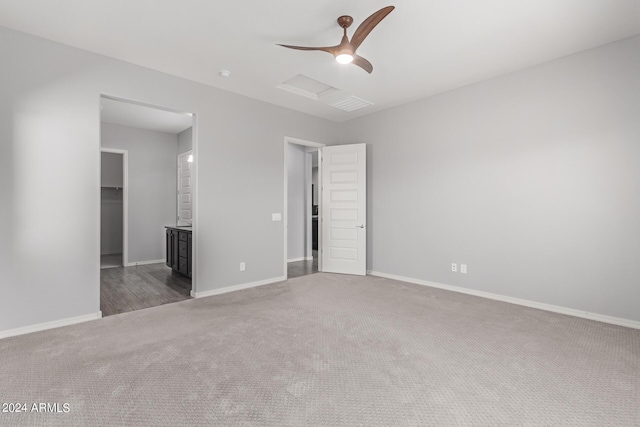 carpeted empty room with attic access, baseboards, and ceiling fan