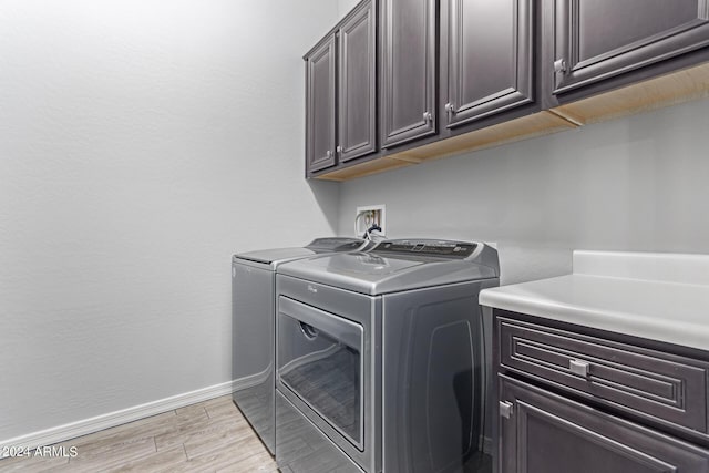 laundry area featuring baseboards, cabinet space, light wood finished floors, and washing machine and clothes dryer