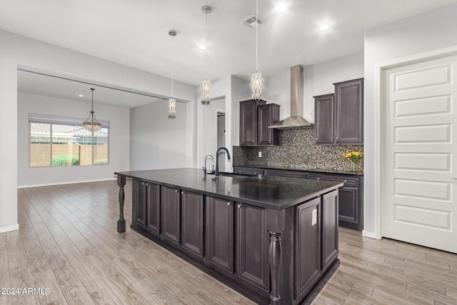 kitchen with dark countertops, light wood-style flooring, a sink, wall chimney range hood, and backsplash