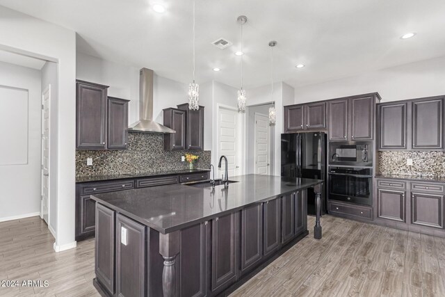 kitchen featuring a center island with sink, black appliances, light hardwood / wood-style flooring, and wall chimney exhaust hood