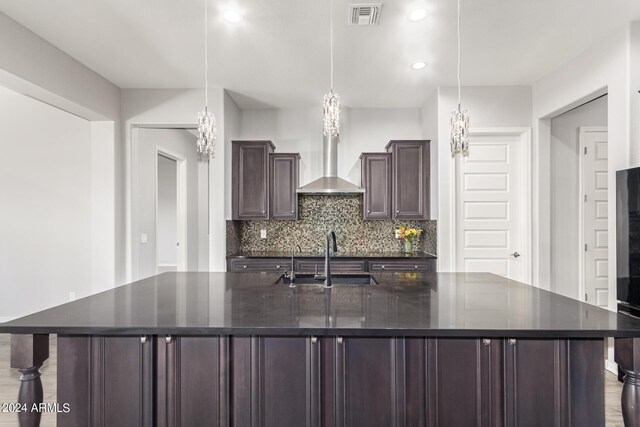 kitchen featuring visible vents, backsplash, a sink, dark brown cabinetry, and wall chimney range hood