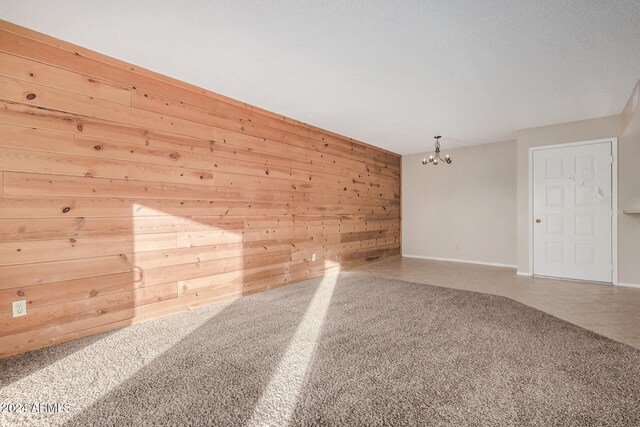 carpeted empty room featuring wooden walls, a chandelier, and a textured ceiling